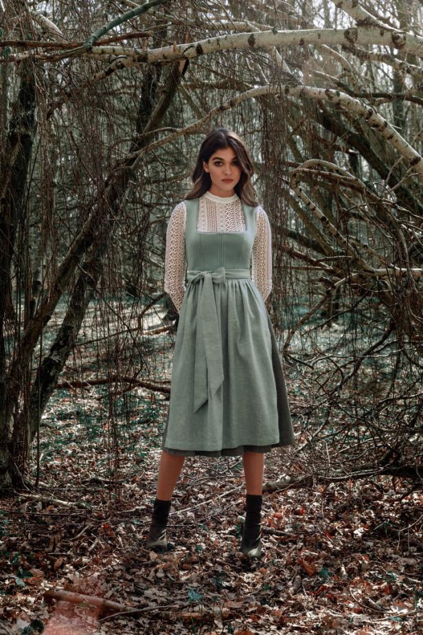 Eine Frau in einem Dirndl steht in einem Wald.