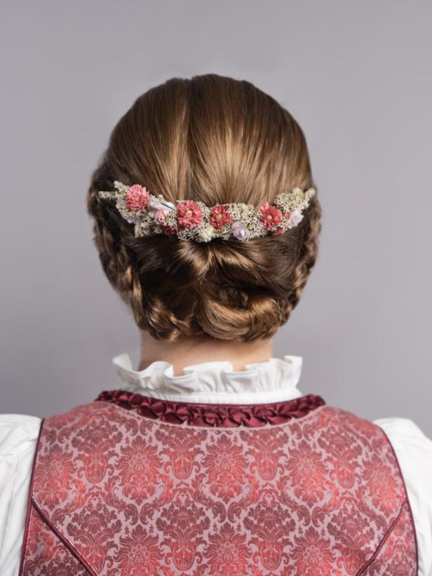 Eine Frau mit geflochtenem Haar und einem Blumenkranz im Haar trägt ein Dirndl.
