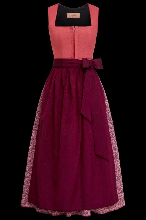 Ein Dirndl mit einem korallfarbenen Oberteil und einem weinroten Rock mit Schleife.