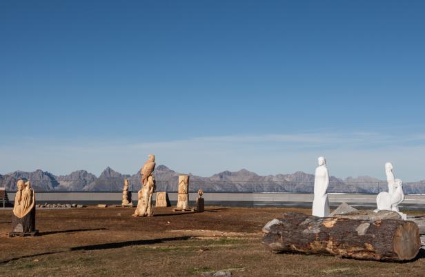 Holz- und Marmorskulpturen stehen auf einer Anhöhe mit Blick auf die Berge.