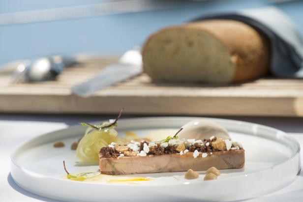 Ein Teller mit einer Pastete, garniert mit Käse und Croutons, dazu Brot im Hintergrund.
