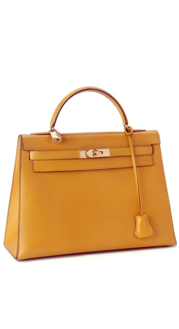 Eine goldene Hermès Kelly Bag steht auf einem weißen Hintergrund.