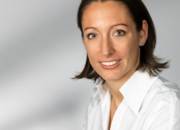 Eine Frau mit braunen Haaren und einem weißen Hemd lächelt.