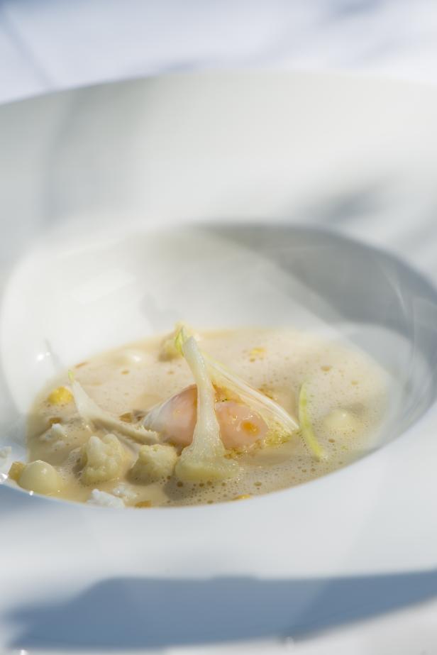 Eine Nahaufnahme einer Schale mit einer hellen Suppe, Blumenkohl und einem pochierten Ei.