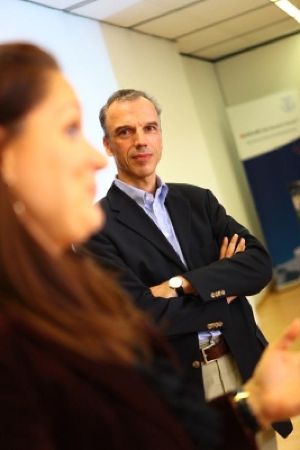 Ein Mann mit verschränkten Armen steht im Hintergrund einer Frau während einer Besprechung.