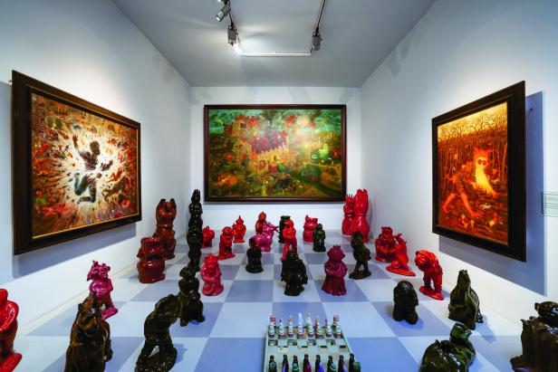 In einem Ausstellungsraum stehen drei Gemälde und ein Schachspiel mit skulpturalen Figuren.