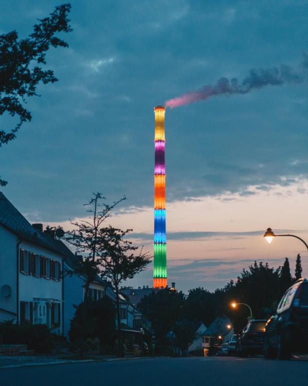 Ein hoher Schornstein ist im Dunkeln mit bunten Lichtern beleuchtet.