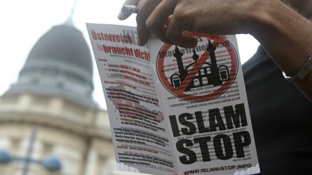 Eine Person hält ein Flugblatt mit der Aufschrift „Islam Stop“ vor einem Gebäude.
