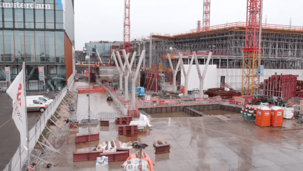 Eine Baustelle in Amsterdam mit mehreren Baukränen und einem Gebäude mit der Aufschrift „amsterdam“.