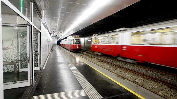 Eine rote und weiße Straßenbahn fährt in einer U-Bahn-Station ein.