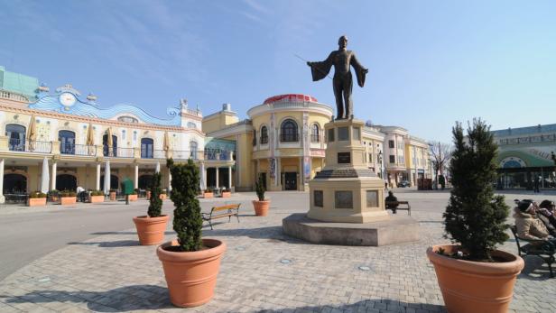 Eine Statue von Johann Strauss steht im Wiener Prater vor bunten Gebäuden.
