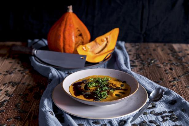 Eine Schüssel Kürbissuppe mit Kürbiskernen und Kräutern auf einem Holztisch.