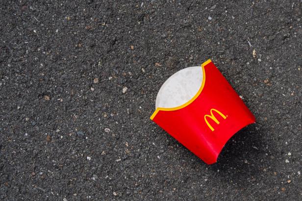 Eine leere Pommes-Verpackung von McDonald's liegt auf dem Asphalt.