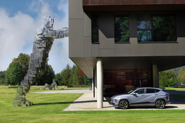 Ein silberner Hyundai Kona steht vor einem modernen Gebäude mit einer Würfel-Skulptur.