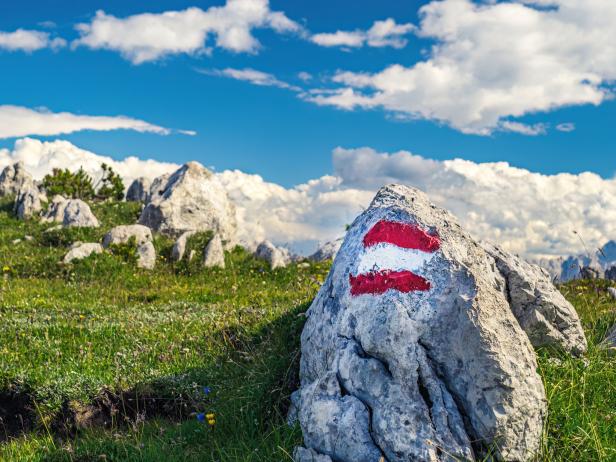 Ein Wegweiser mit rot-weiß-roter Markierung auf einem Felsen in den Bergen.