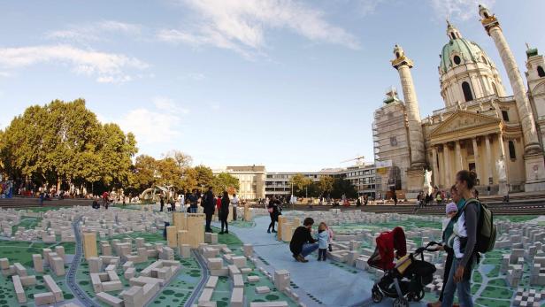 Menschen besuchen eine Installation mit einem Stadtmodell auf dem Karlsplatz in Wien.