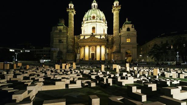 Die Karlskirche in Wien ist nachts hell erleuchtet, im Vordergrund eine Installation aus Betonquadern.