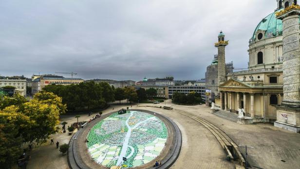 Blick auf den Karlsplatz in Wien mit der Karlskirche und einem Stadtplan-Mosaik im Vordergrund.