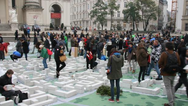 Menschen interagieren mit einer Installation aus weißen Blöcken, die ein Stadtbild darstellen.