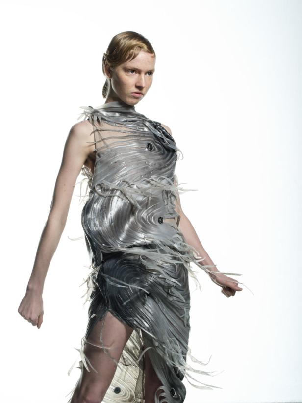 Eine Frau präsentiert ein futuristisches Kleid aus schimmernden, fließenden Materialien.