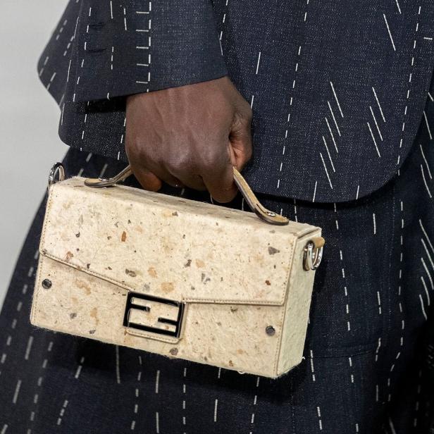 Eine Person hält eine Fendi-Handtasche aus beigem Papier mit dunklen Sprenkeln.