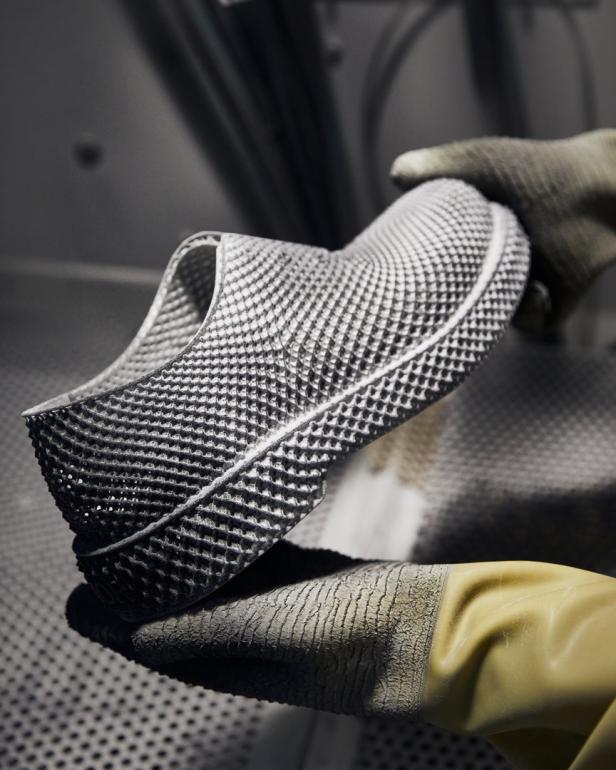 Ein 3D-gedruckter Schuh wird von behandschuhten Händen gehalten.