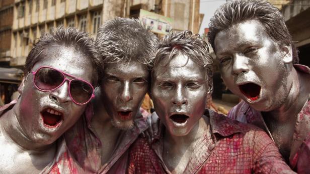 Vier Männer mit silberbemalter Haut schreien in die Kamera.