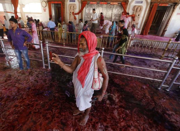 Ein Mann mit rotem Tuch macht ein Foto in einem Tempel, dessen Boden mit Farbe bedeckt ist.