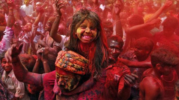 Eine Menschenmenge feiert das Holi-Fest mit roter Farbe bedeckt.