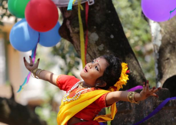 Ein junges Mädchen in traditioneller Kleidung tanzt vor einem Baum mit bunten Luftballons.
