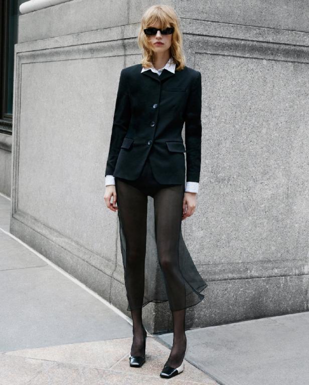 Eine Frau mit Sonnenbrille trägt einen schwarzen Blazer und transparente Leggings.