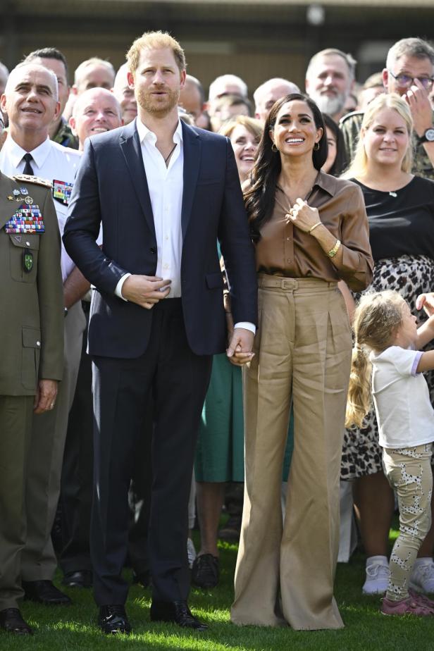 Prinz Harry und Meghan Markle halten Händchen inmitten einer Menschenmenge.