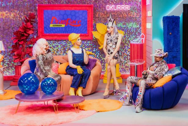 Vier Dragqueens sitzen in einem farbenfrohen Studio von „Drag Race Germany“.
