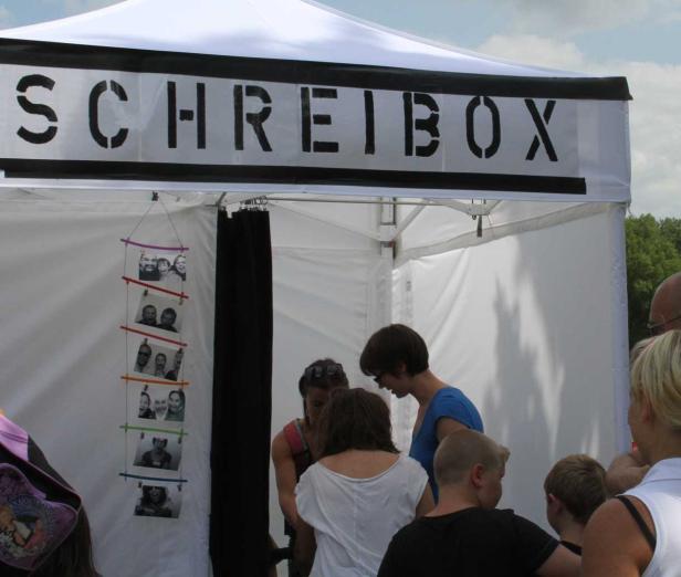 Menschen stehen vor einer „Schreibox“ auf einem Festival.