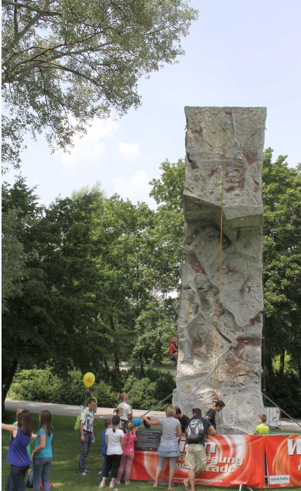 Eine mobile Kletterwand steht auf einer Wiese, umgeben von Zuschauern.