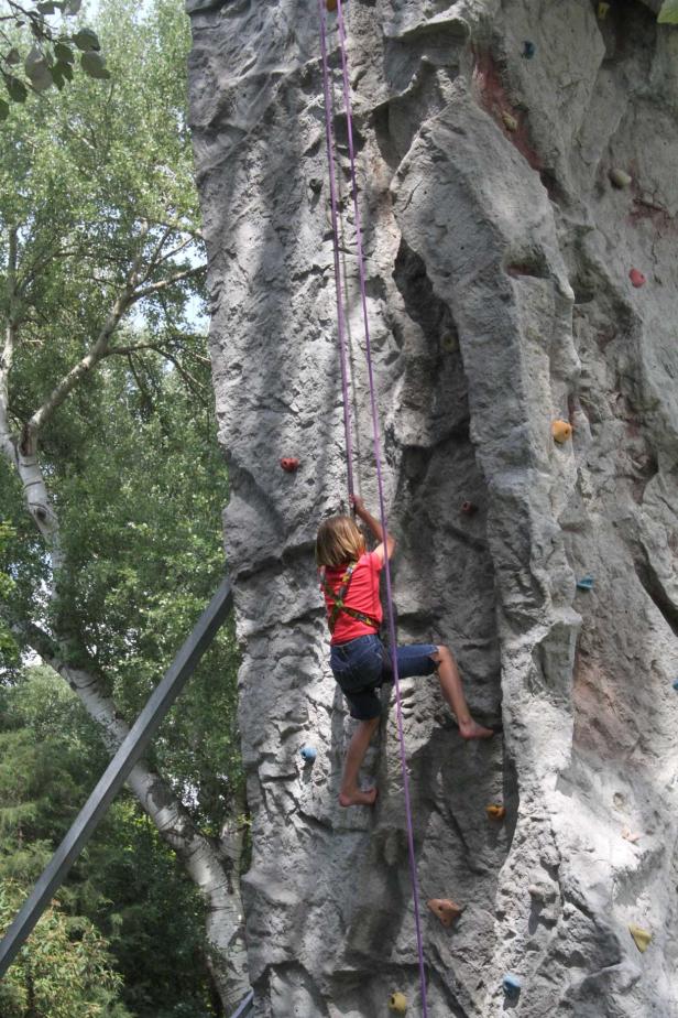 Ein Mädchen klettert barfuß an einer künstlichen Felswand mit Klettergriffen.