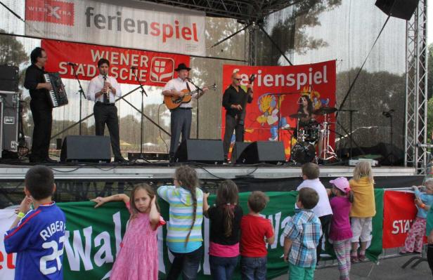 Eine Band spielt auf einer Bühne vor einer Gruppe von Kindern.