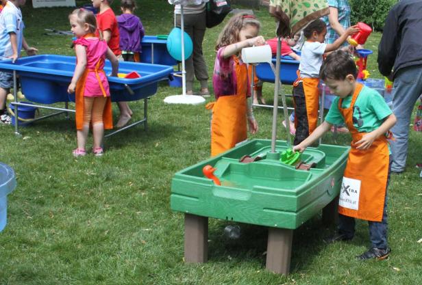 Kinder spielen mit Wasser an verschiedenen Spieltischen im Freien.