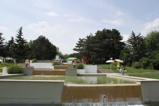 Ein mehrstufiger Brunnen in einem Park mit Menschen im Hintergrund.