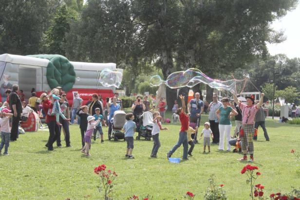 Ein Seifenblasen-Künstler unterhält Kinder auf einer grünen Wiese.