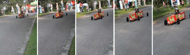 Ein Kind fährt in einem roten Seifenkistenwagen ein Rennen hinunter.