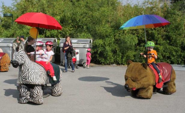Kinder reiten auf motorisierten Zebra- und Bärenspielzeugen im Freien.