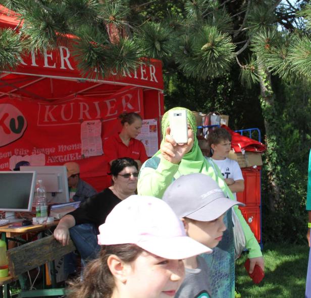 Eine Frau mit Kopftuch fotografiert mit ihrem Smartphone vor einem Stand des „Kurier“.