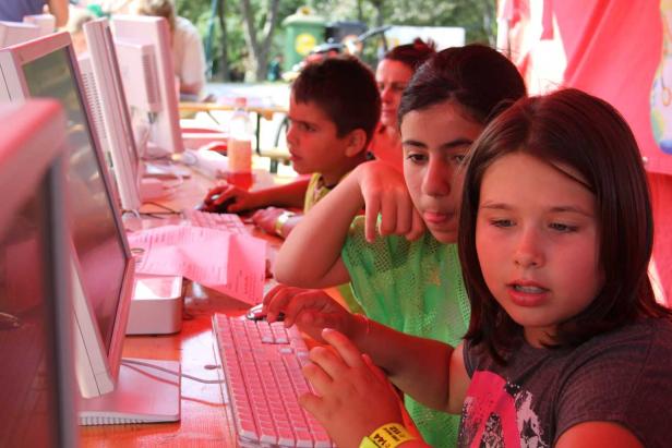 Kinder sitzen an Computern und tippen auf Tastaturen.