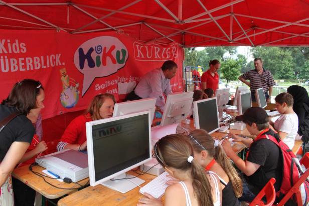 Kinder sitzen an Computern unter einem roten Zelt mit der Aufschrift „KiKu“.