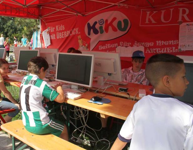 Kinder sitzen an Computern unter einem roten Kiku-Zelt.