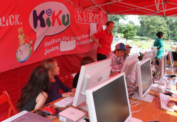 Kinder sitzen an Computern unter einem roten Zelt mit der Aufschrift „KiKu“.