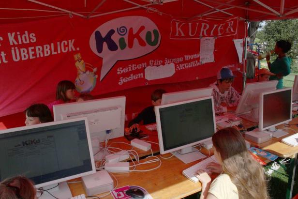 Kinder sitzen an Computern unter einem roten Zelt mit der Aufschrift „KiKu Kurier“.