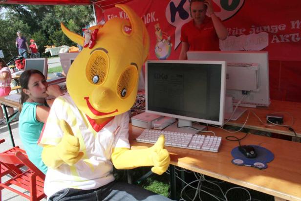 Ein gelbes Maskottchen gibt vor einem Computerbildschirm einen Daumen nach oben.