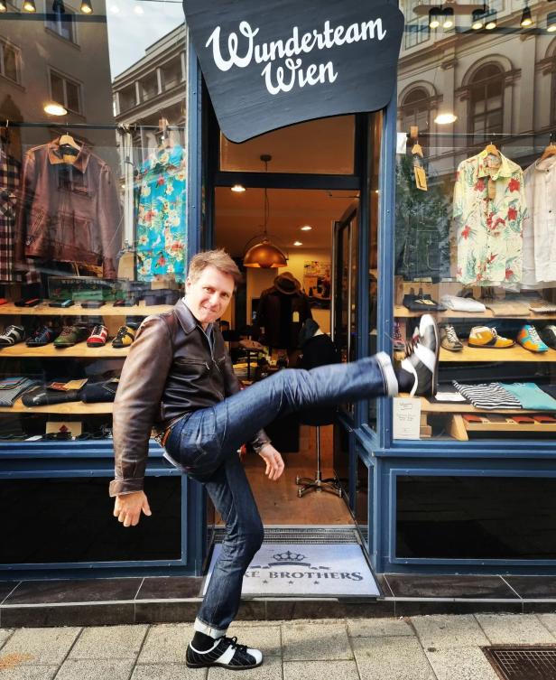Ein Mann posiert vor dem „Wunderteam Wien“ Geschäft und streckt ein Bein aus.